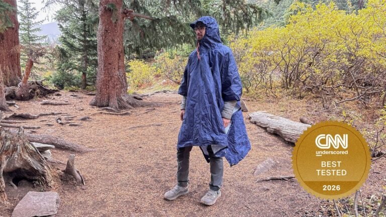 A bright yellow rain poncho for hiking draped over a mossy forest boulder.