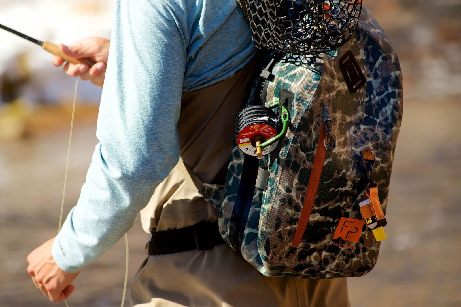 A functional fishing sling bag sitting on a wooden dock by a lake.