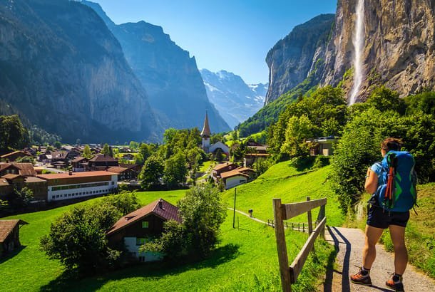 Hiker on a green alpine trail with snowy Swiss peaks during the best time to visit Switzerland for hiking