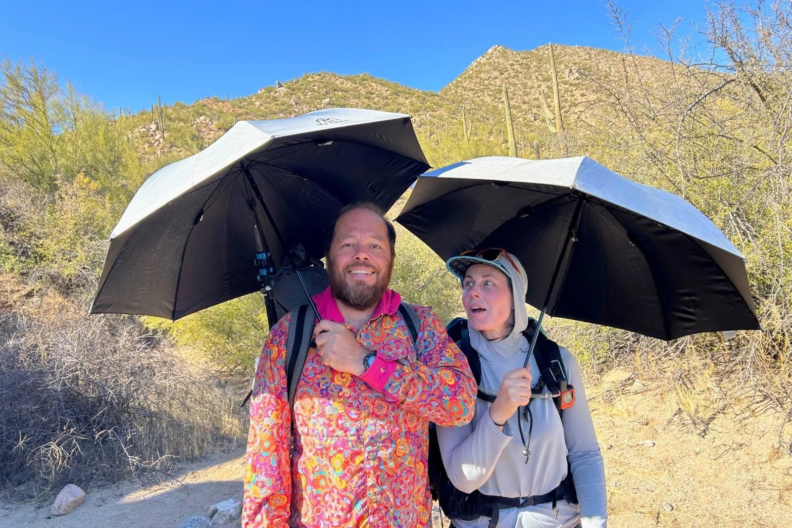 A hiker uses a durable trekking umbrella while walking on a mountain trail.