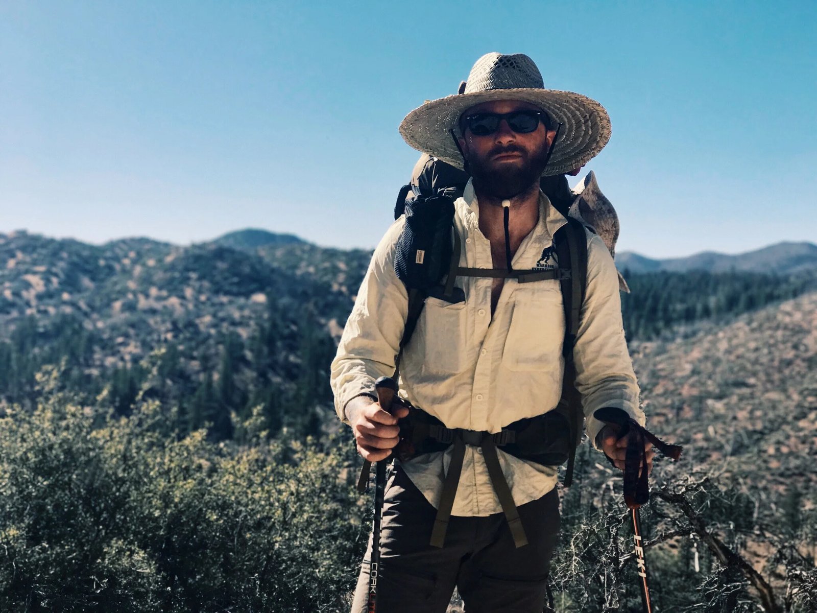 A hiker wearing a wide-brimmed hat on a sunny mountain trail.