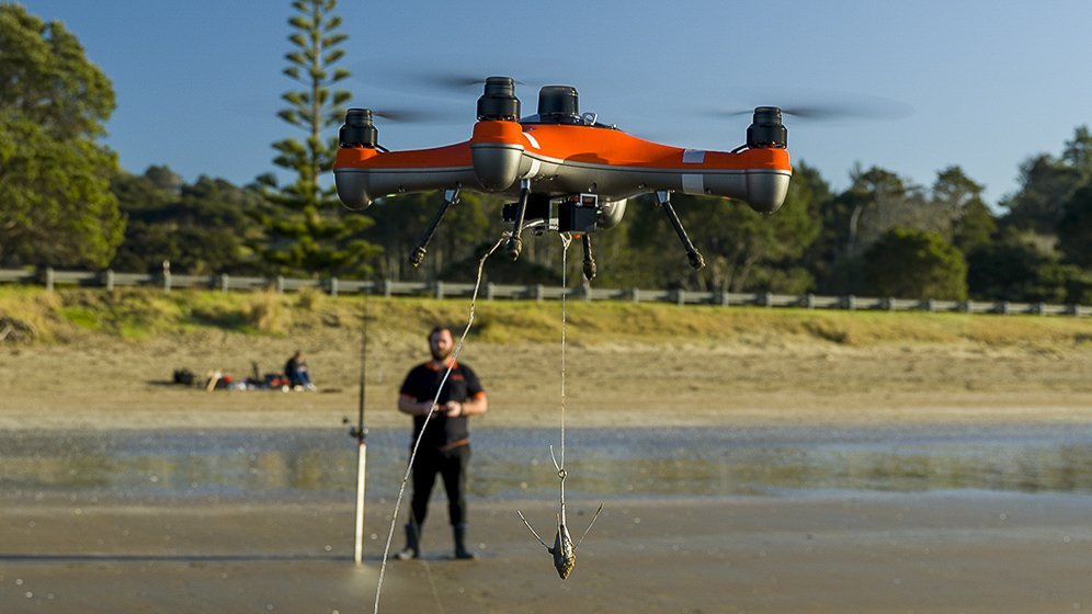 A modern fishing drone hovers over calm ocean water to drop bait.