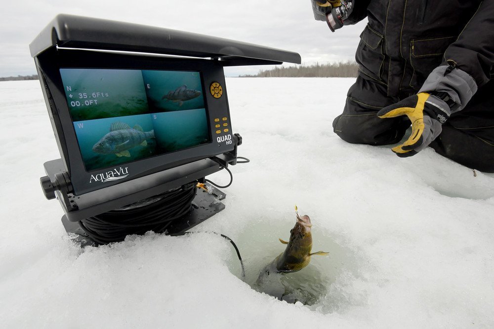A modern ice fishing camera sits on a frozen lake beside an open hole.