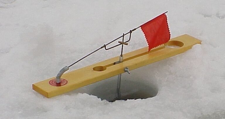 An orange ice fishing tip-up sits on a frozen lake during a winter morning.