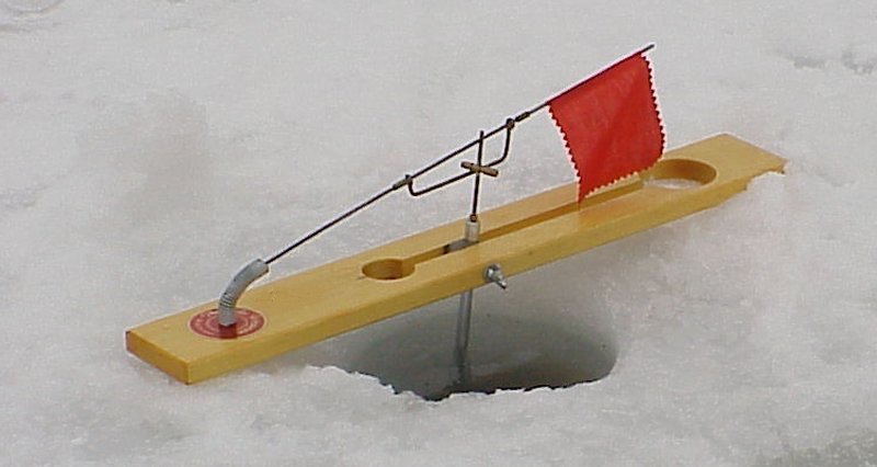 An orange ice fishing tip-up sits on a frozen lake during a winter morning.