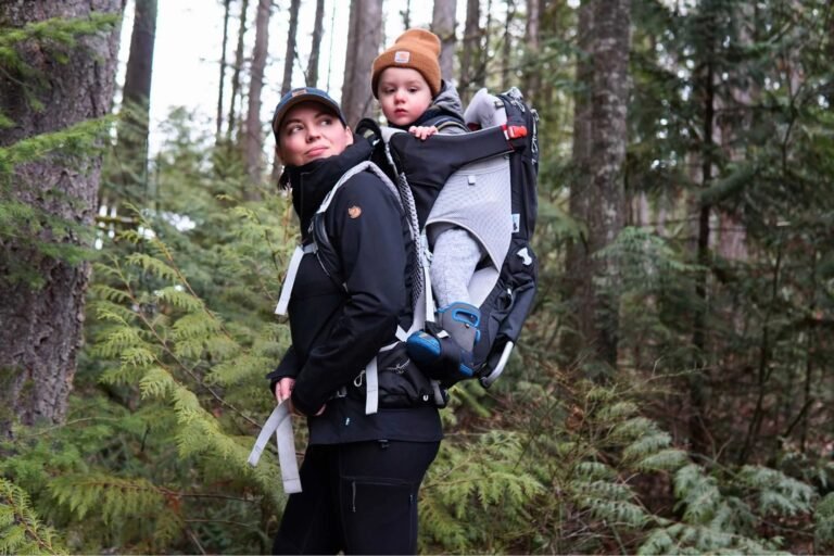 A parent hikes a forest trail wearing a baby carrier for hiking.