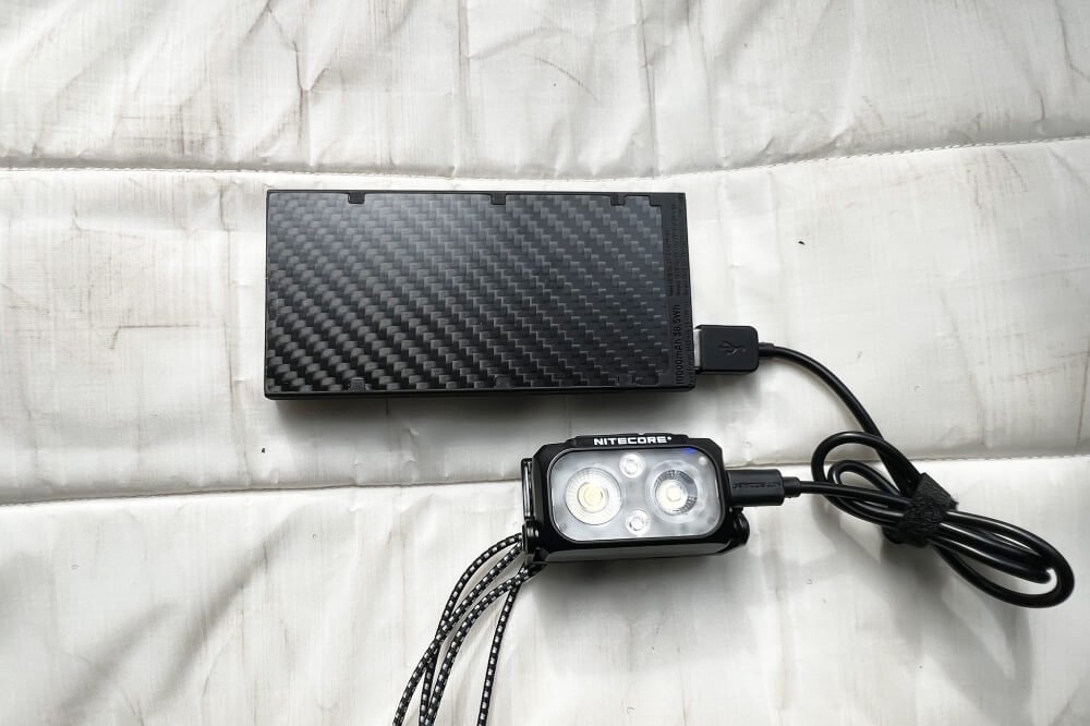 A rugged power bank for hiking resting on a mountain trail rock.