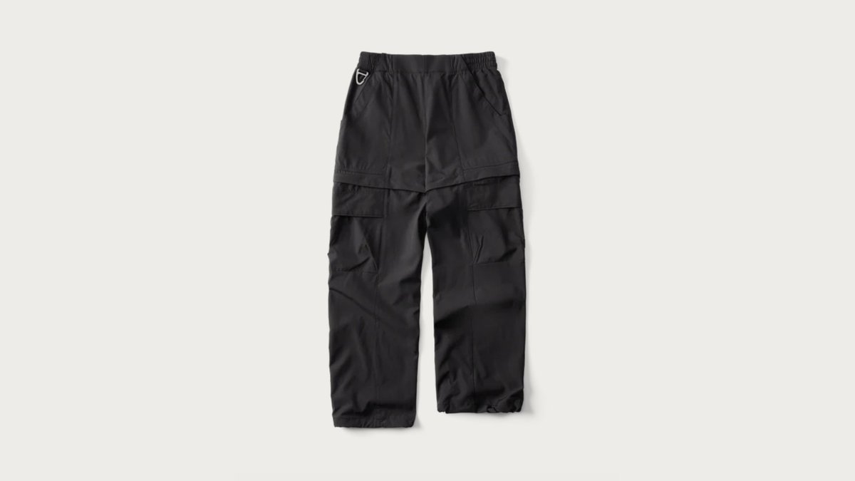 A tall hiker wearing comfortable hiking pants stands on a scenic mountain ridge.