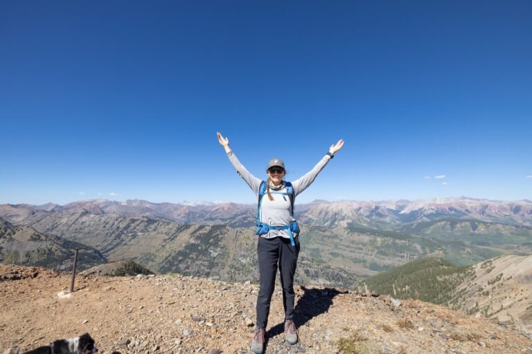 A woman wearing functional hiking clothes stands on a mountain ridge during sunset.