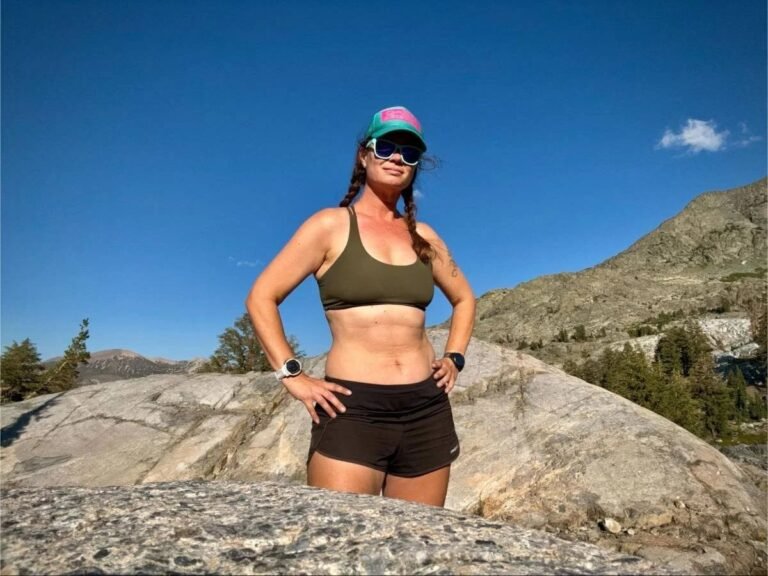 A woman wearing a supportive hiking bra stands on a mountain ridge at sunrise.